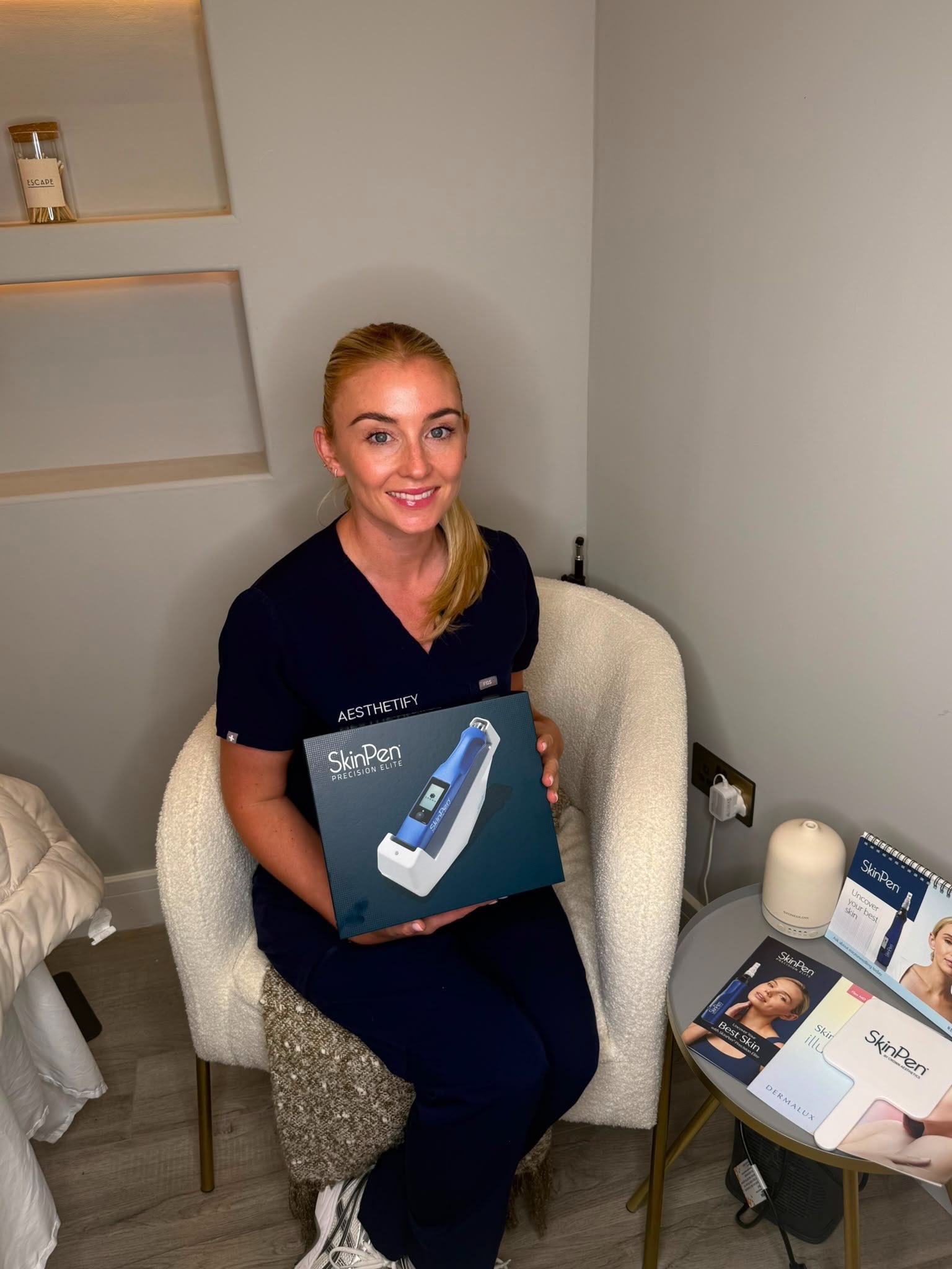 Lauren Brady, registered nurse, seated in the clinic in navy Aesthetify scrubs and holding a SkinPen box